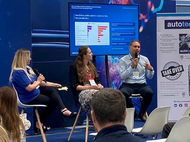 Two women and a man sat on high seats speaking into microphones to interested audience